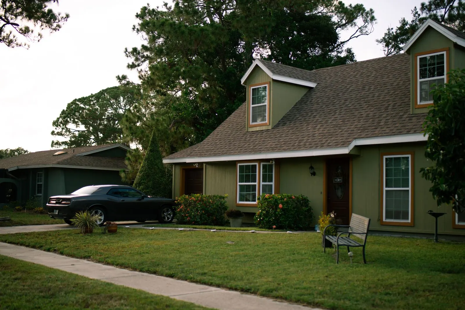 Olive green American house with a front lawn, shrubs and a car parked in the driveway