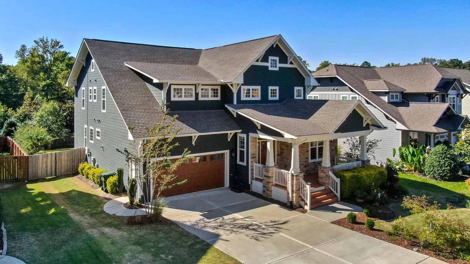Two story craftsman style house with dark green siding, stone porch columns and a wide concrete driveway