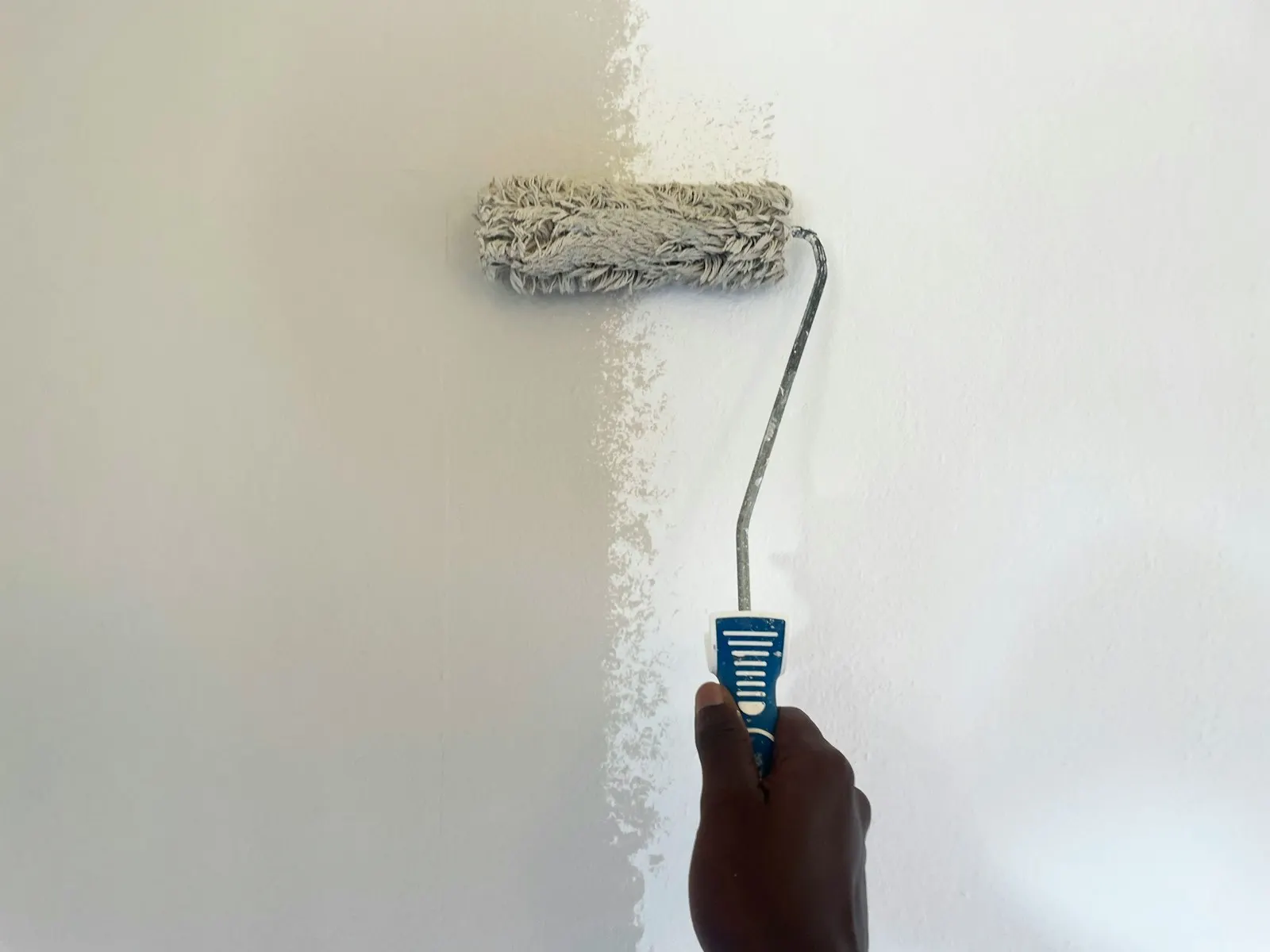 Close up of a hand rolling fresh paint onto an interior wall